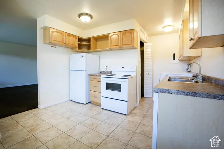 Kitchen featuring tile flooring, wood-finish cabinetry, laminate countertops, a double basin stainless steel sink, and white appliances