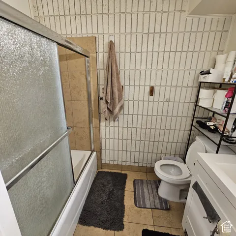 Bathtub with sliding glass enclosure, ceramic tile flooring, and white vanity with built-in storage