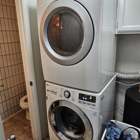 Stackable washer and dryer, white cabinetry, and tiled wall