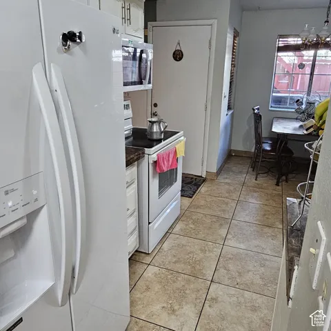 Kitchen featuring a white refrigerator, a white electric range with a microwave above, built-in white cabinetry, and tile flooring
