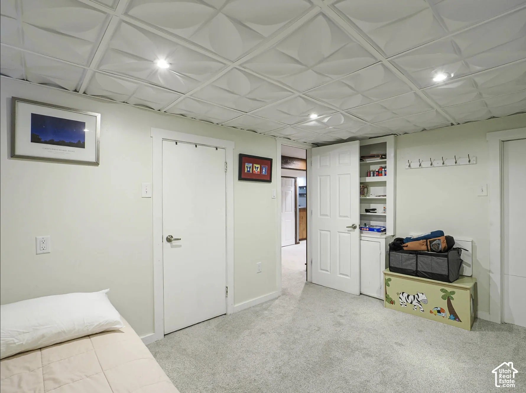 Recessed lighting illuminates the textured ceiling tiles, complemented by light gray carpeting and white walls