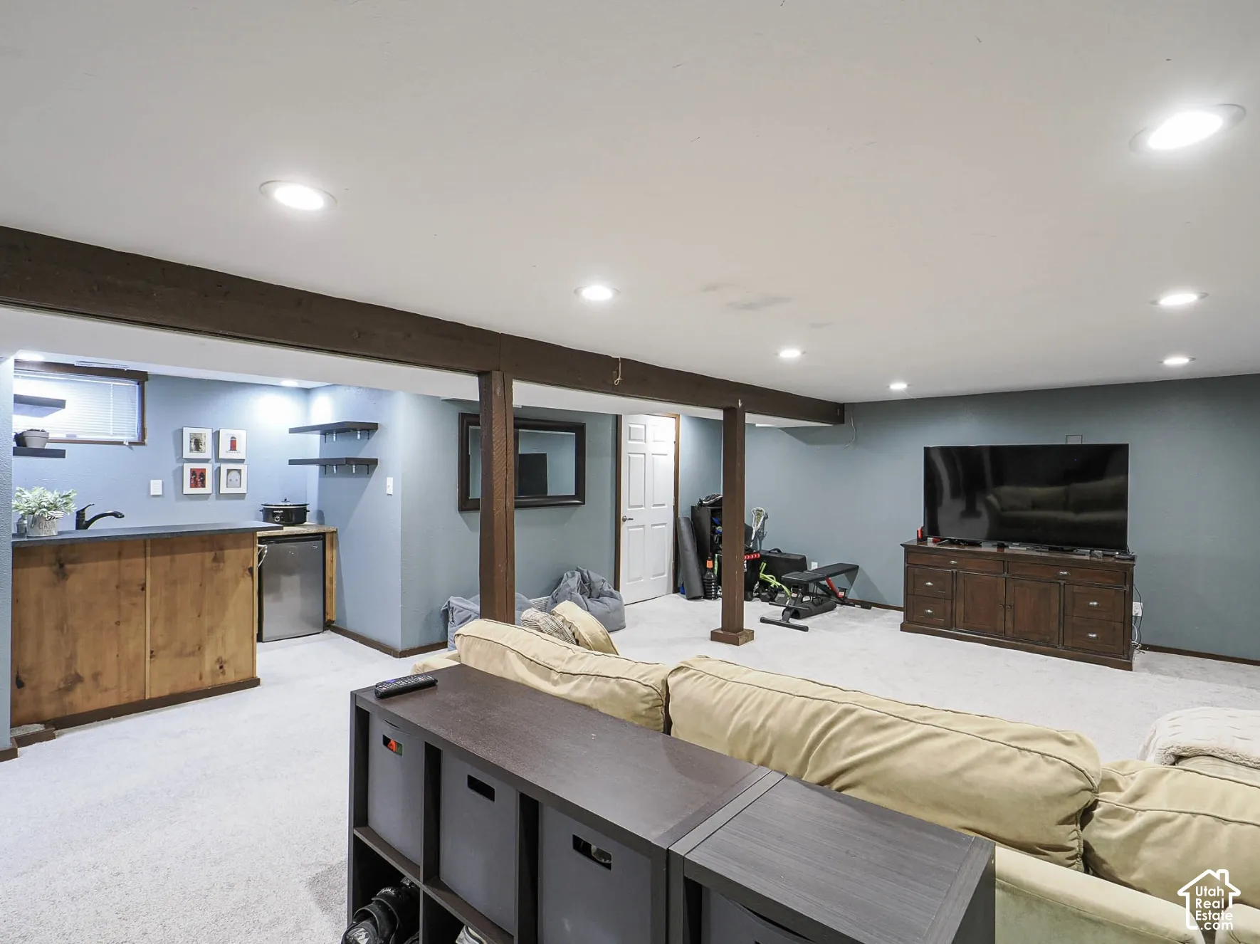 Recessed lighting throughout, exposed wood-finish beams, integrated wet bar with sink, mini-refrigerator, and wall-mounted shelving