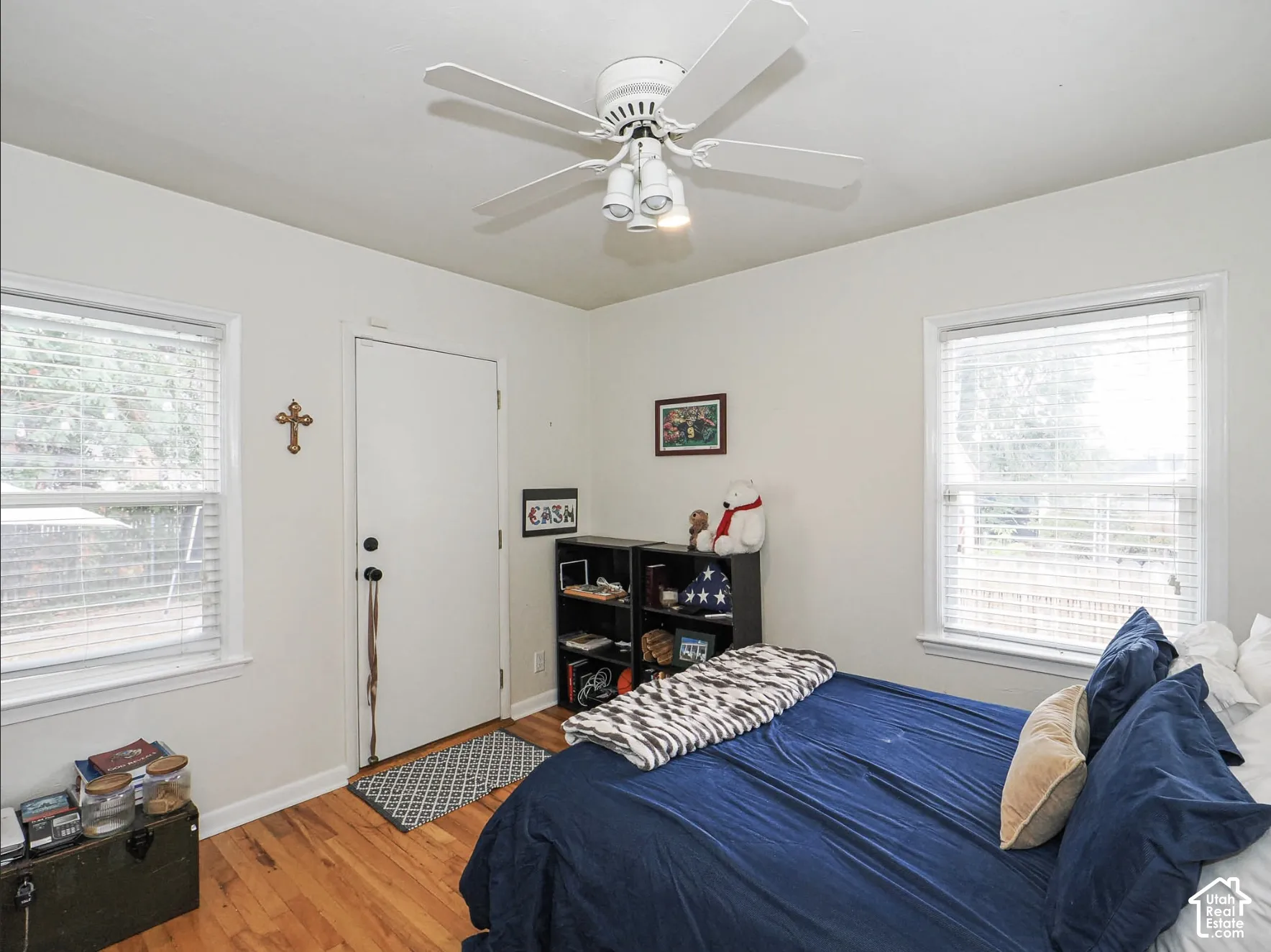 Hardwood flooring, white painted walls, white ceiling fan with integrated lighting, two windows with blinds