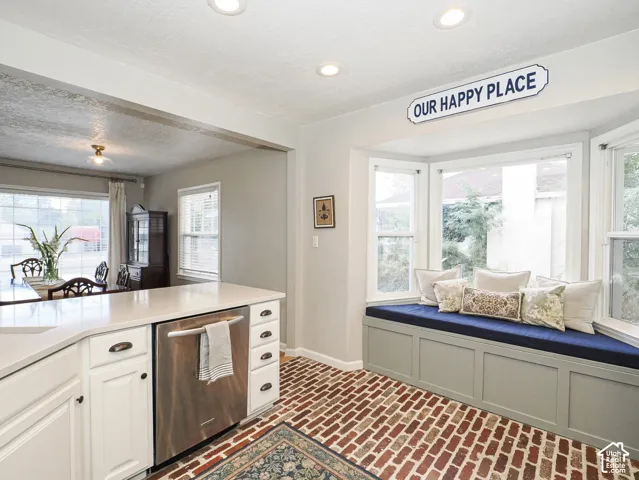 Built-in window bench with multi-pane windows, brick-patterned flooring, recessed ceiling lighting, and white cabinetry with a light-toned countertop