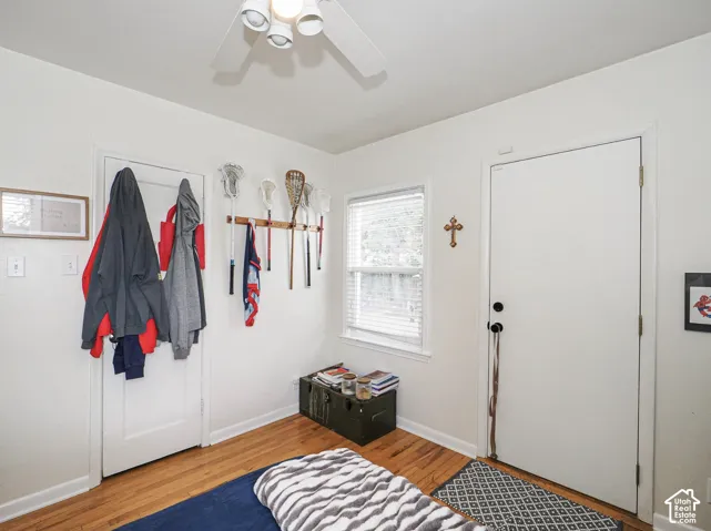 Hardwood flooring, ceiling fan, white paneled door, window with blinds, white wall finish