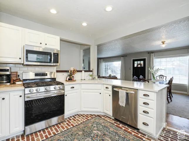 White cabinetry, stainless steel appliances, brick-finish flooring, white subway tile backsplash, and recessed lighting
