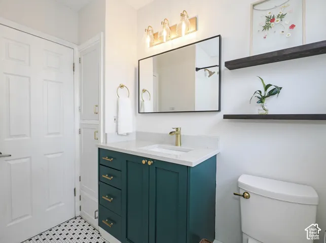 Vanity with a white countertop and gold-finish faucet, framed mirror, wall-mounted light fixture, built-in shelving, and hexagonal floor tiling
