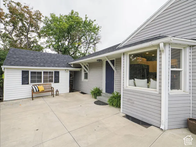 Concrete patio area with a dark blue entry door, bay window, and a white siding exterior