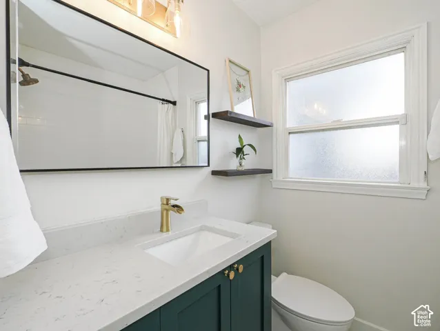 Bathroom featuring a dark green vanity with gold-finish hardware, a white countertop, a rectangular undermount sink, a gold-finish faucet, and a large rectangular mirror