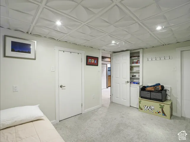 Recessed lighting illuminates the textured ceiling tiles, complemented by light gray carpeting and white walls