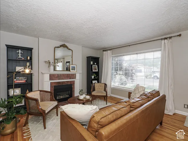 Hardwood flooring, fireplace with brick surround and white mantel, two built-in shelving units, and a large window with blinds