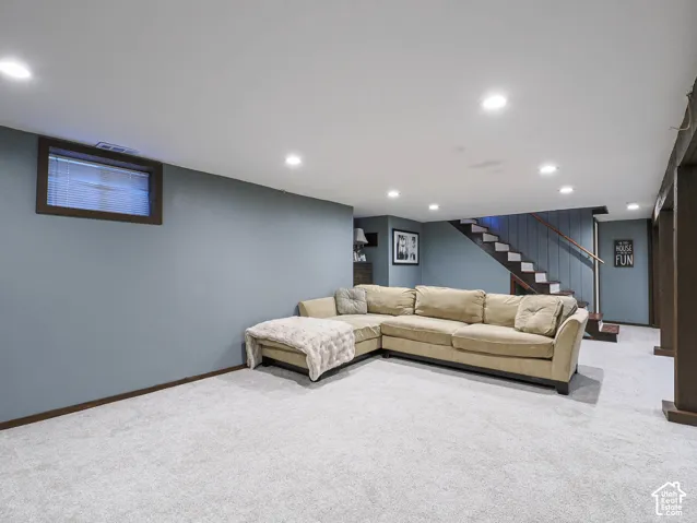 Recessed lighting, light gray carpeting, window with blinds, painted walls, and staircase with wood handrail