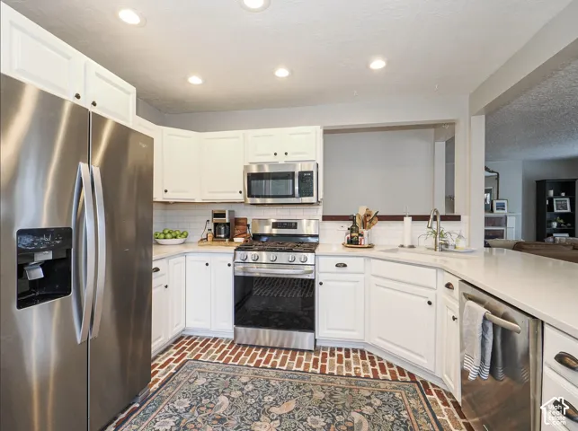 Kitchen featuring stainless steel appliances, white cabinetry, a tile backsplash, light-toned countertops, and brick-finish flooring