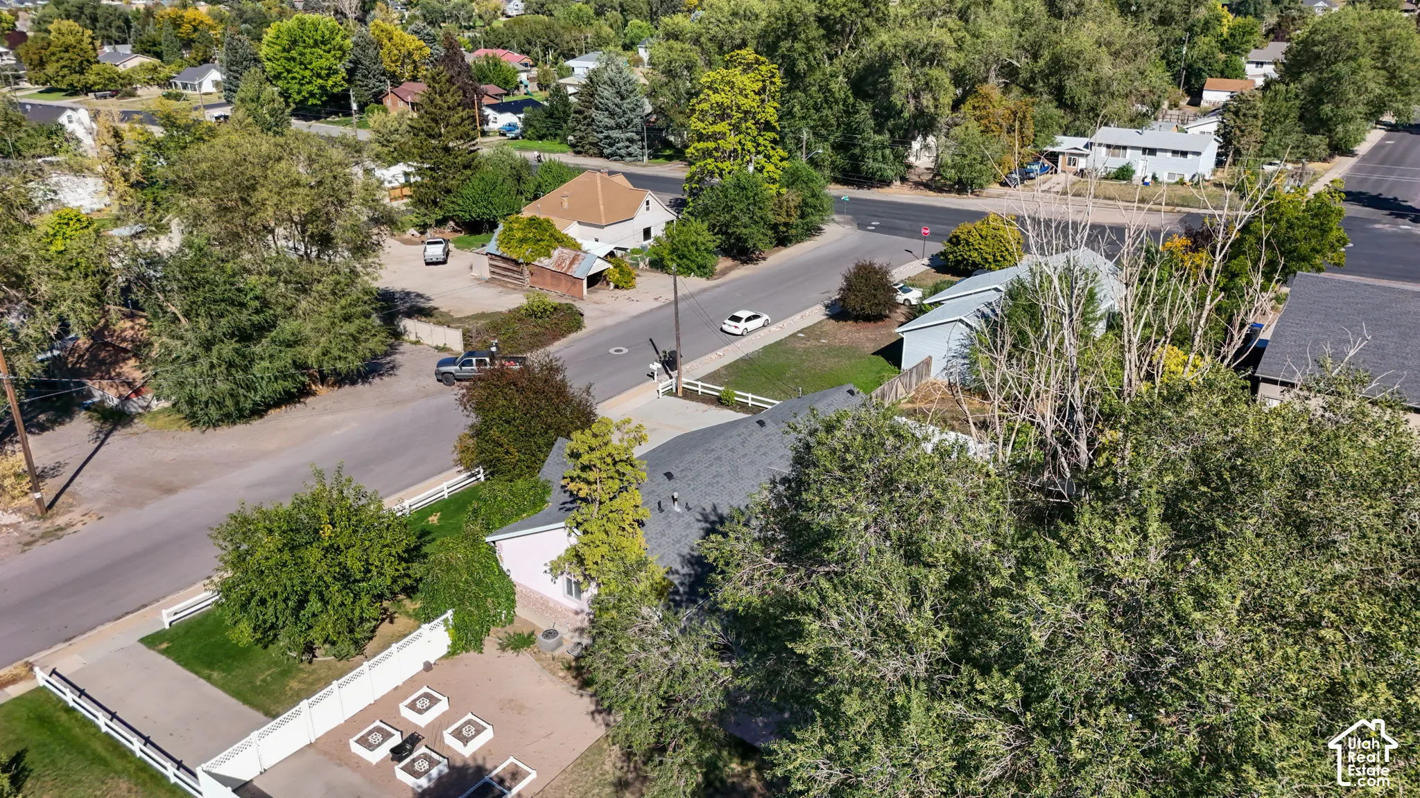 Residential property featuring a paved driveway, white privacy fencing, and surrounding mature trees