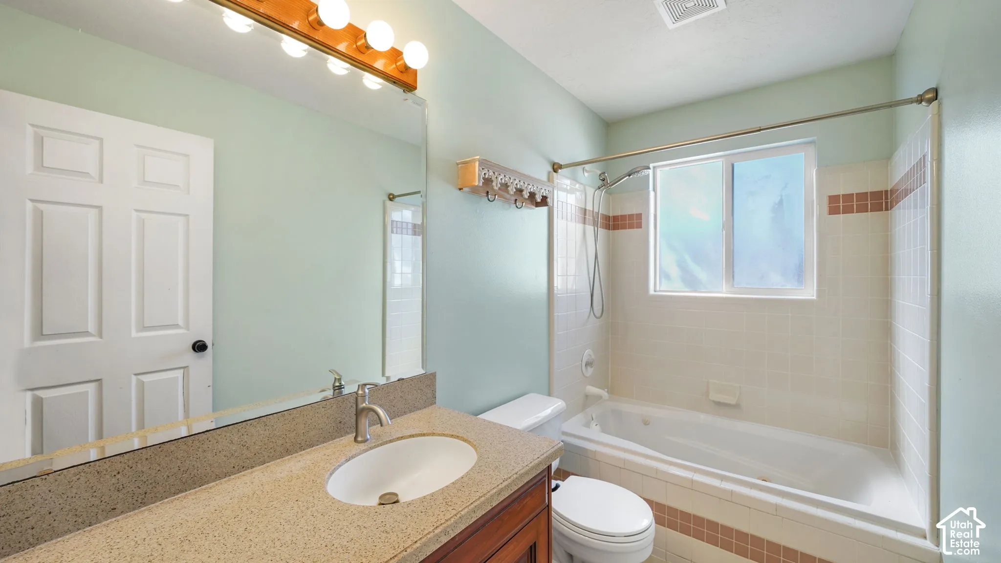 Bathroom featuring a vanity with an integrated sink, a large wall-mounted mirror, a tub with a shower fixture, and a window