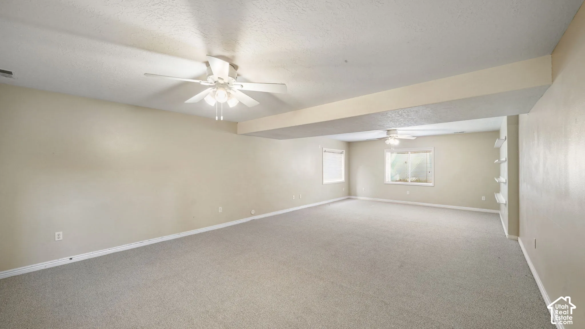 Expansive room featuring neutral wall tones, carpeted flooring, two ceiling fans, and built-in shelving
