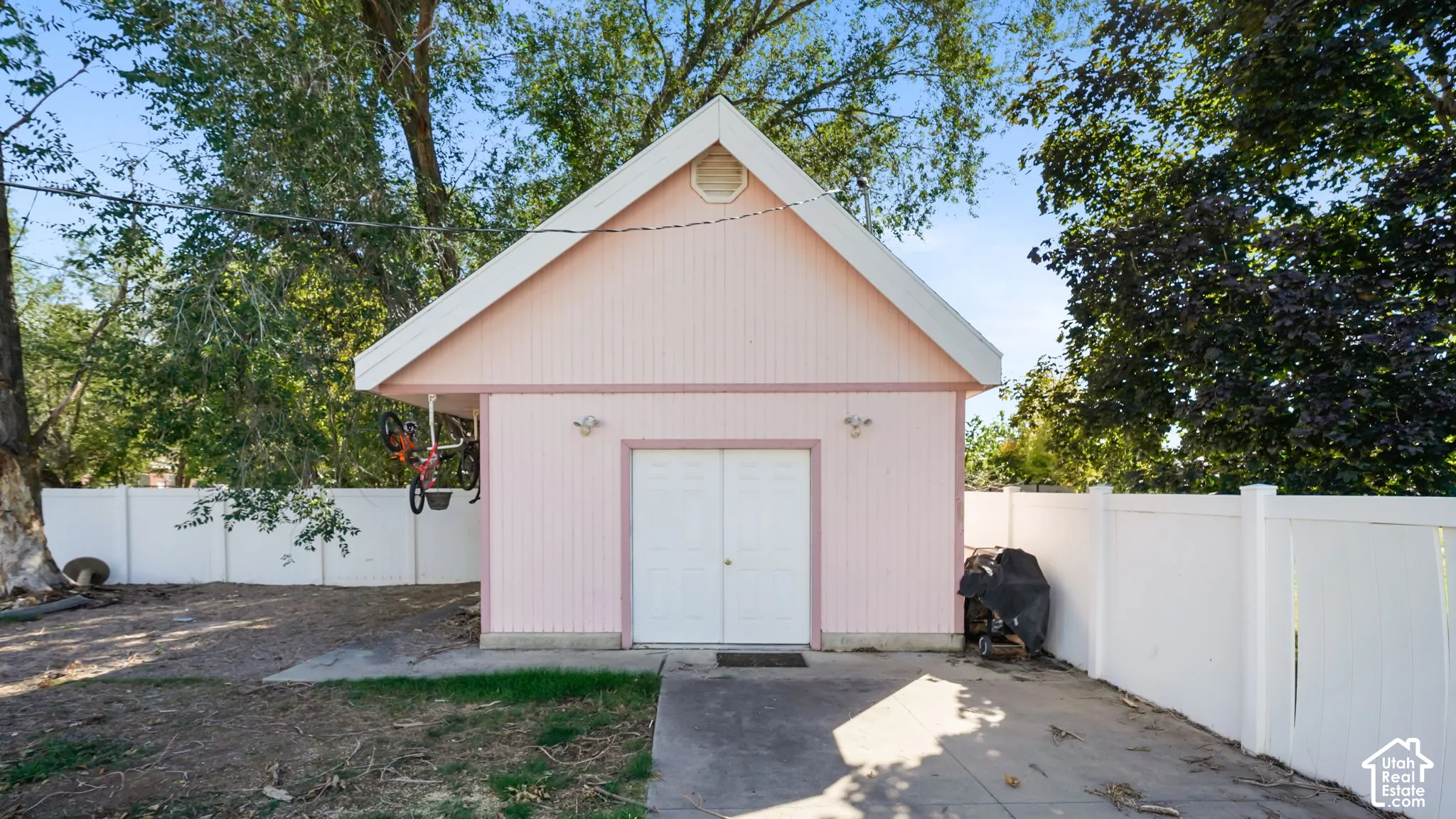 Detached shop featuring a gabled roofline, double entry doors, two exterior light fixtures, and a white privacy fence