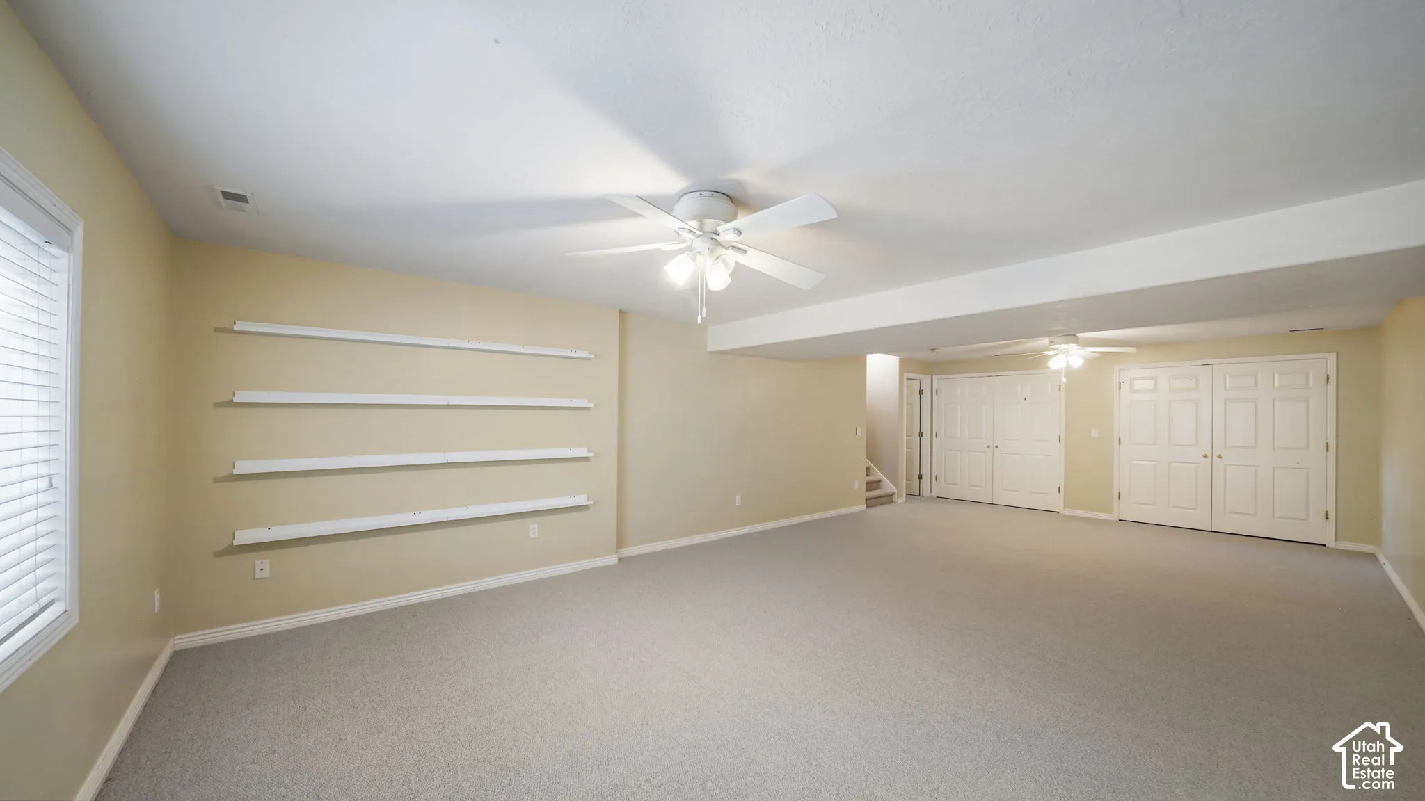 Spacious room with light-colored carpeting, multiple ceiling fans, and built-in shelving units
