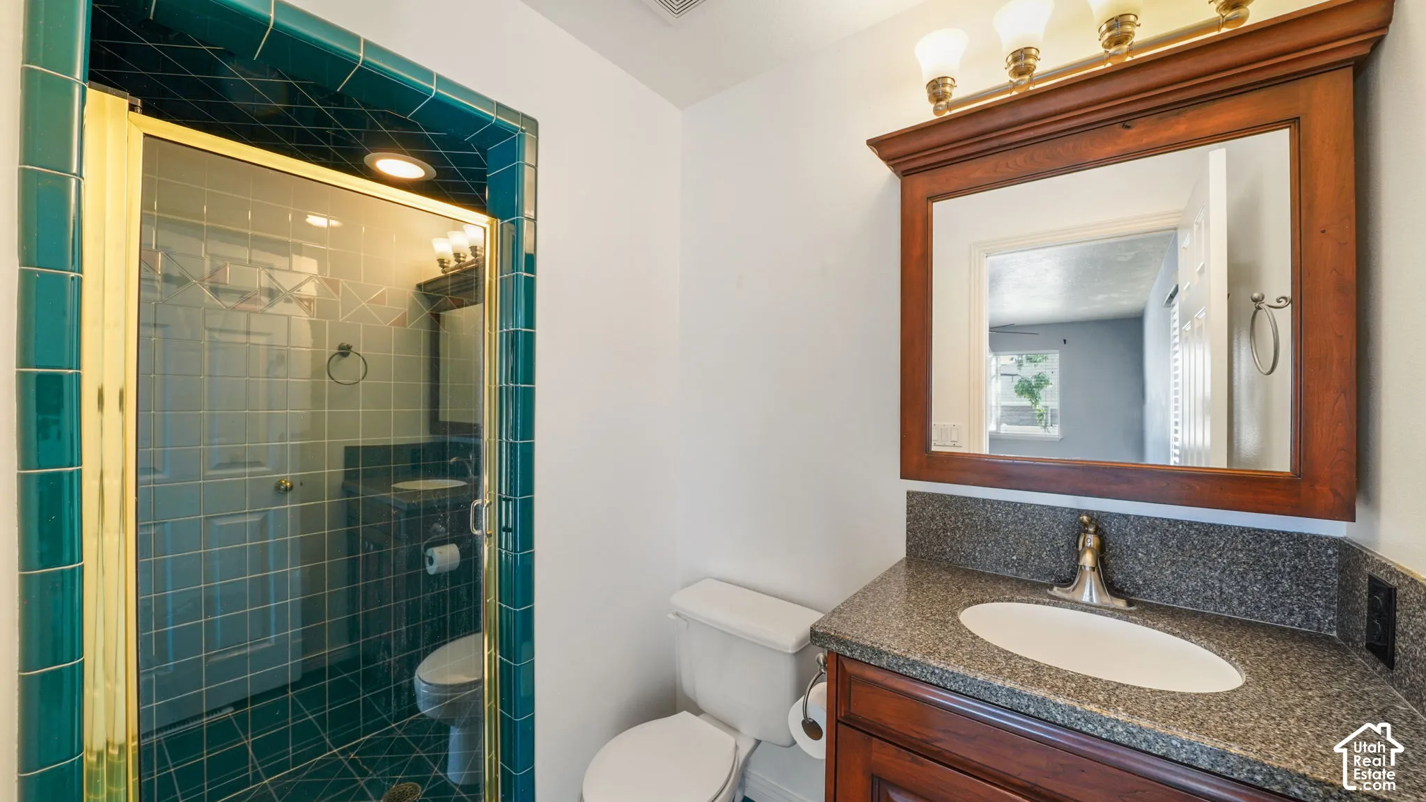 Primary bathroom featuring a wood-finish vanity with an integrated sink, a dark speckled countertop, and a framed mirror with an overhead light fixture