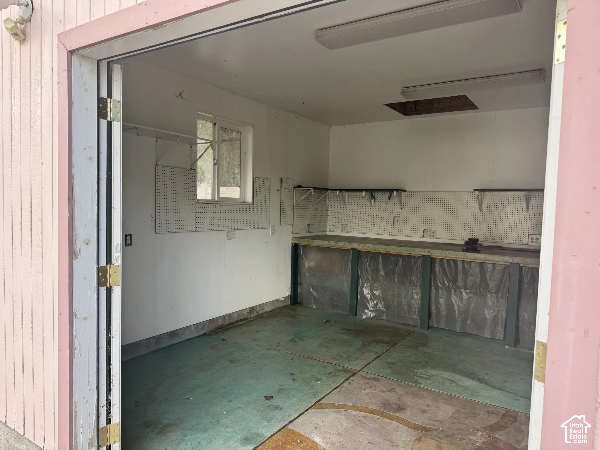 Shop space featuring a window, built-in shelving, pegboard walls, and concrete flooring