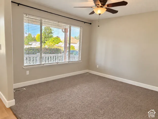 Neutral wall paint, soft carpet flooring, wide window with blinds, and a ceiling fan with integrated lighting