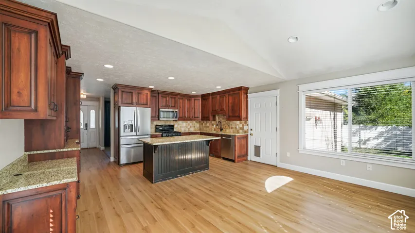 Open-concept kitchen with wood-finish flooring, recessed lighting, and a vaulted ceiling