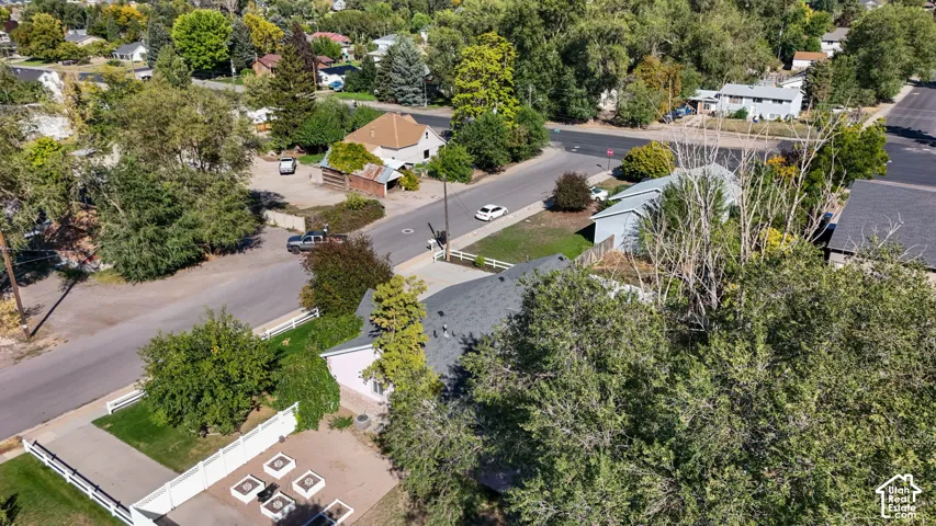 Residential property featuring a paved driveway, white privacy fencing, and surrounding mature trees