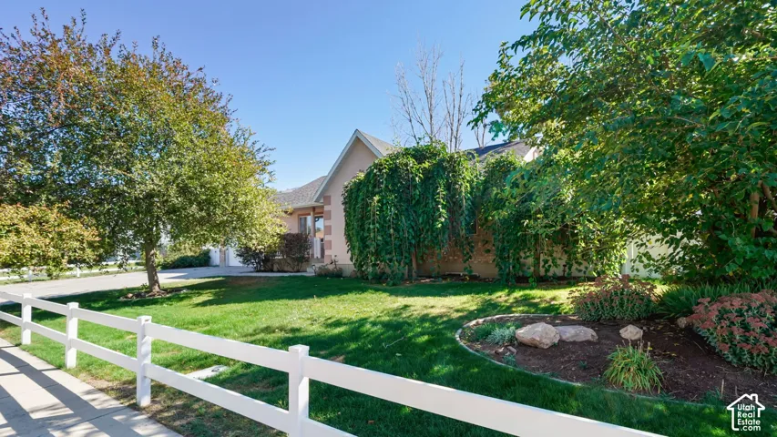 Manicured front yard featuring a white fence, mature trees, and landscaped garden beds
