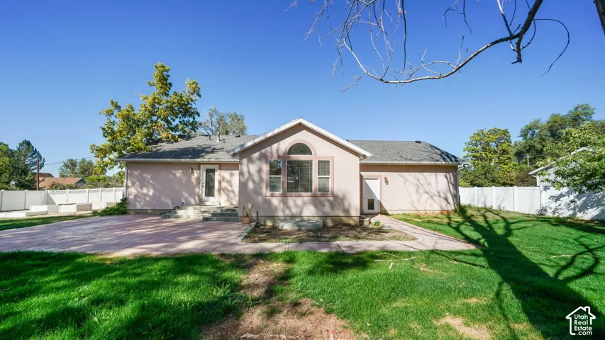 Expansive backyard featuring a manicured lawn, a large patio area, and white privacy fencing