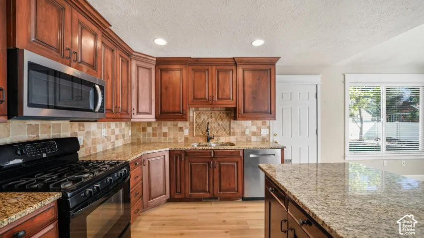 Rich wood cabinetry, stainless steel appliances, granite countertops, tile backsplash, and light wood-finish flooring