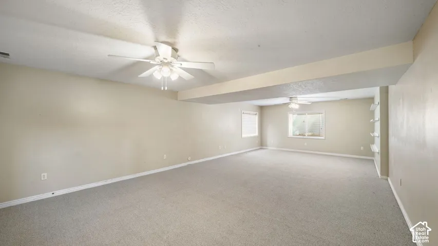 Expansive room featuring neutral wall tones, carpeted flooring, two ceiling fans, and built-in shelving