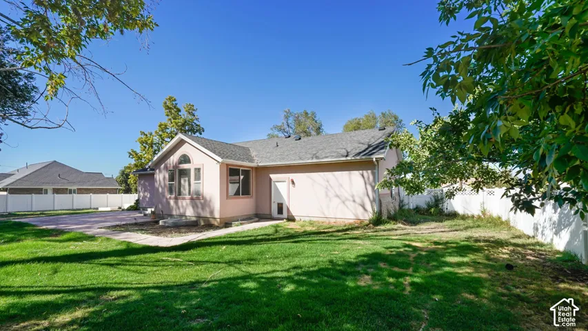 Expansive grassy area with concrete patio, enclosed by a white privacy fence