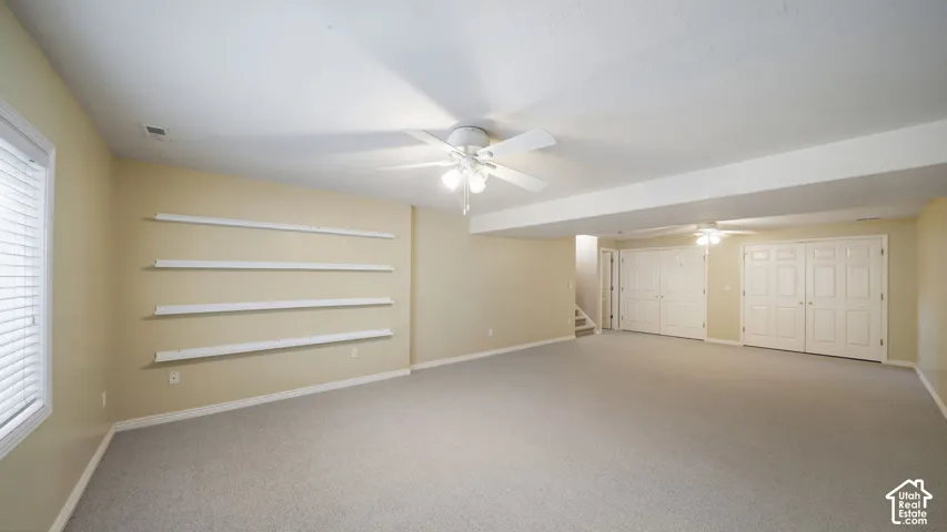 Spacious room with light-colored carpeting, multiple ceiling fans, and built-in shelving units