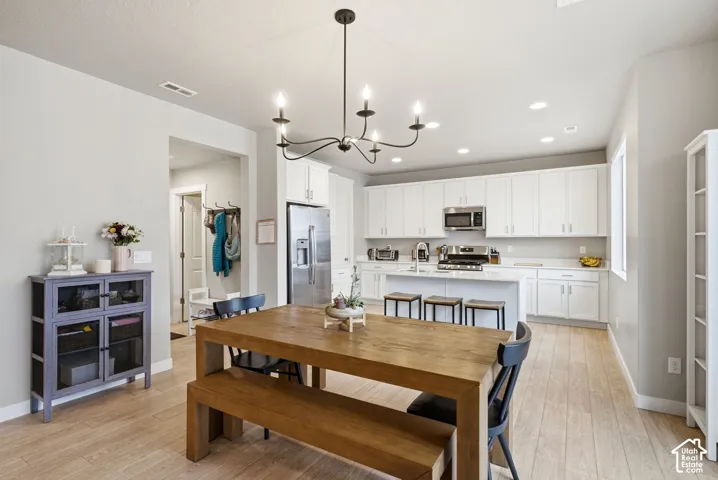 Open-concept kitchen and dining area featuring light-toned wood-finish flooring, white cabinetry, stainless steel appliances, and a central island with counter seating