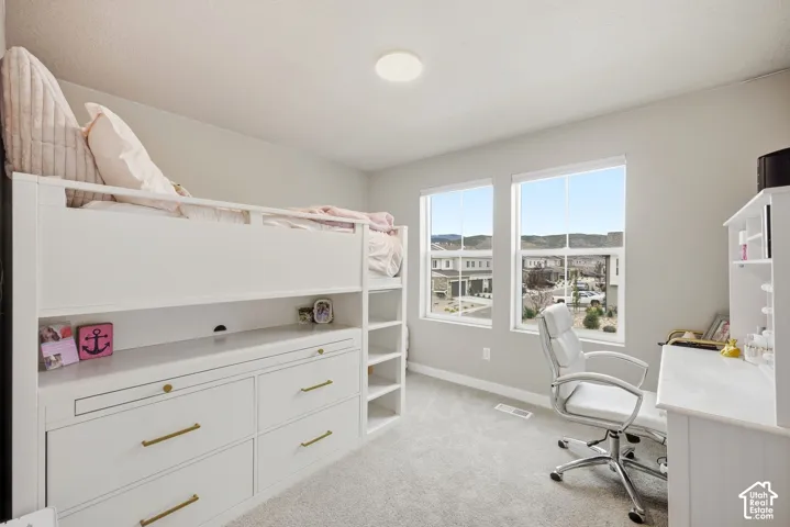 Light gray wall paint, two large windows, white window trim, light gray carpeting, and a round flush-mount ceiling light fixture