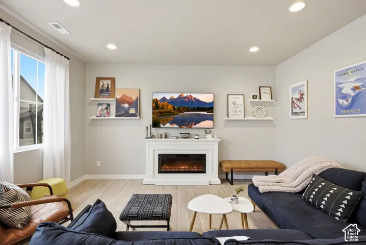 Recessed lighting, light wood-finish flooring, and a white mantel with an electric fireplace