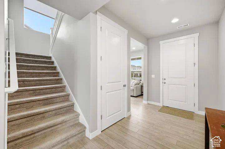 Entryway featuring wood-finish flooring, a white paneled entry door, recessed lighting, and a carpeted staircase with white railings