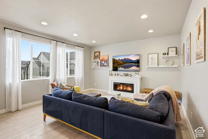 Recessed lighting, wood-finish flooring, large windows, white fireplace with mantle, and floating wall shelves