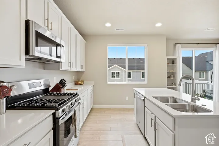 Kitchen featuring white cabinetry, stainless steel appliances, light-toned countertops, a kitchen island with a double basin sink, and wood-finish flooring