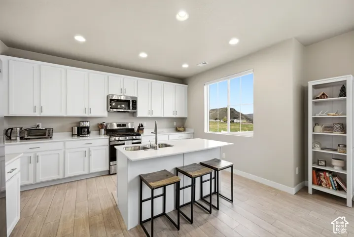 White shaker cabinetry, stainless steel appliances, central island with seating, light wood-finish flooring, and recessed ceiling lighting
