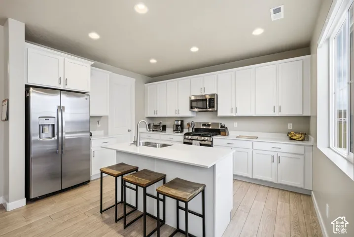 Spacious kitchen featuring white cabinetry, stainless steel appliances, a center island with counter seating, and wood-finish flooring