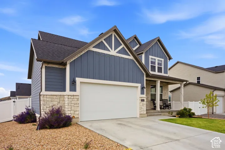 Two-story exterior with vertical siding and stone accents, featuring an attached two-car garage, covered porch, and mature landscaping