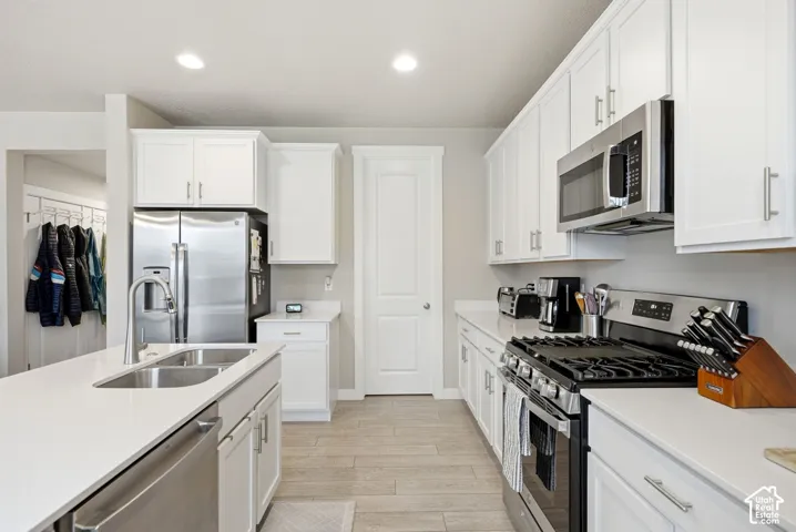 White shaker cabinetry, stainless steel appliances, wood-finish flooring, recessed lighting, and white countertops