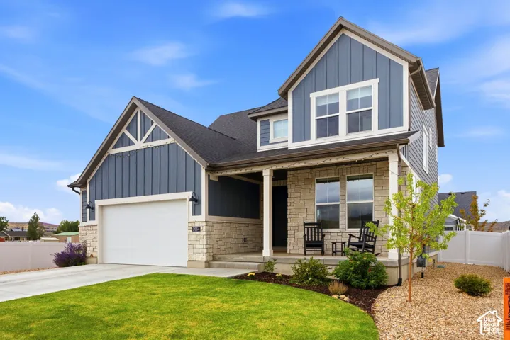 Multi-level residence featuring stone and siding exterior, an attached garage, covered front porch, and manicured landscaping