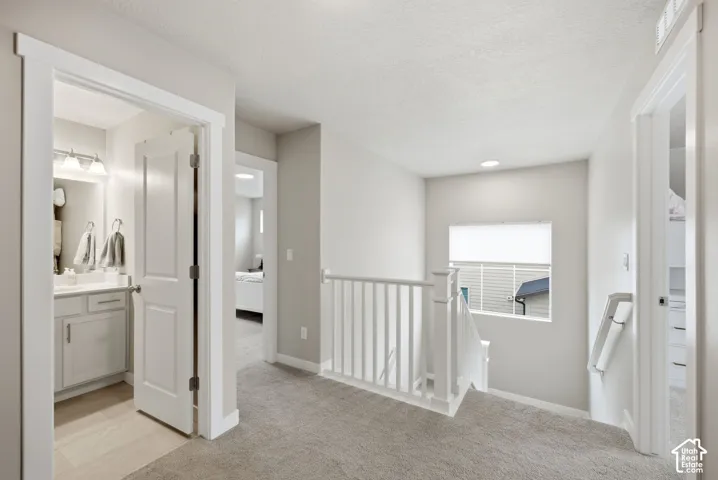 Carpeted landing with white balusters, recessed lighting, and a window with roller shade
