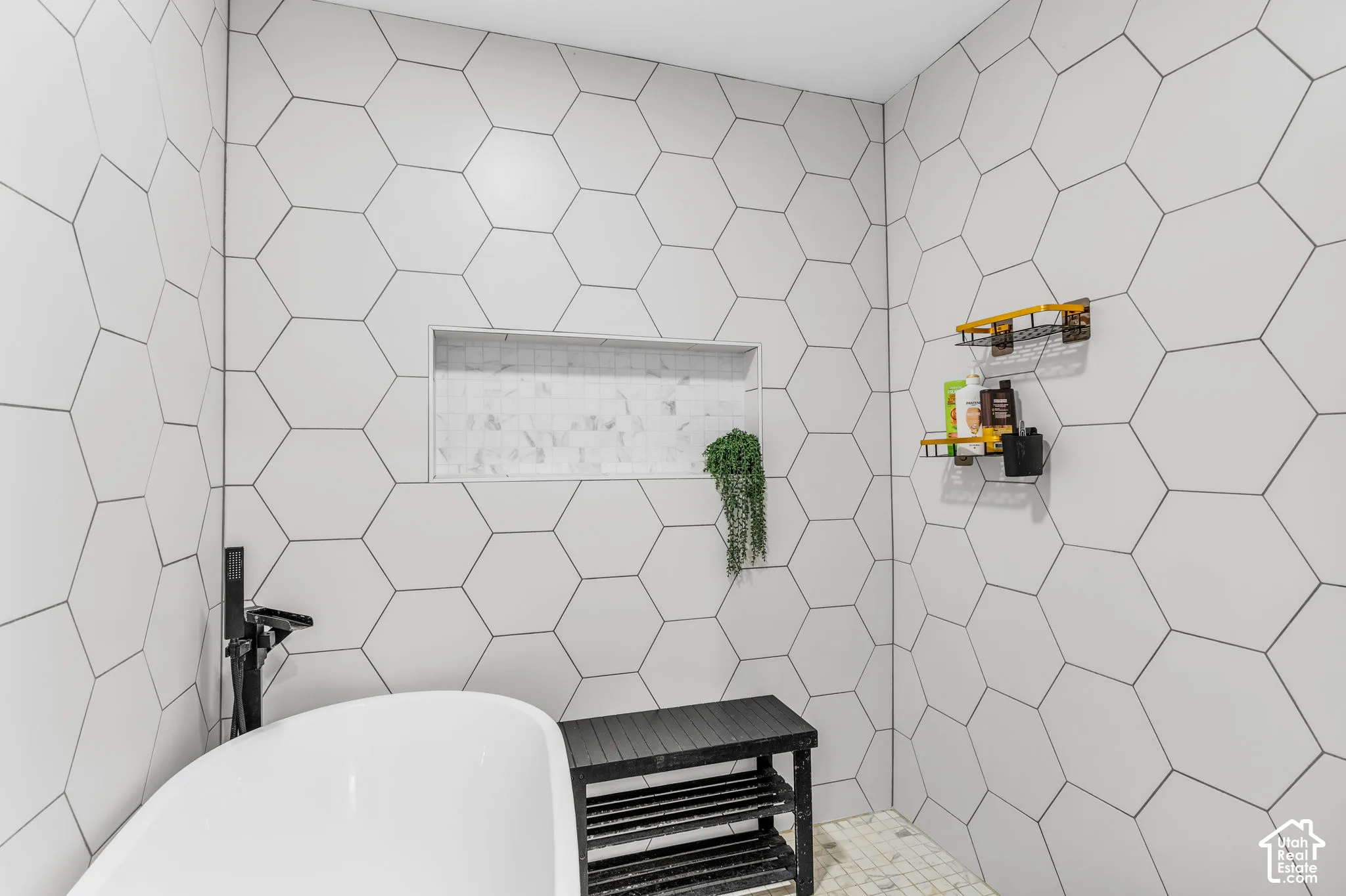 White hexagonal wall tiling, built-in tiled shower niche, and a freestanding soaking tub with a matte black floor-mounted faucet