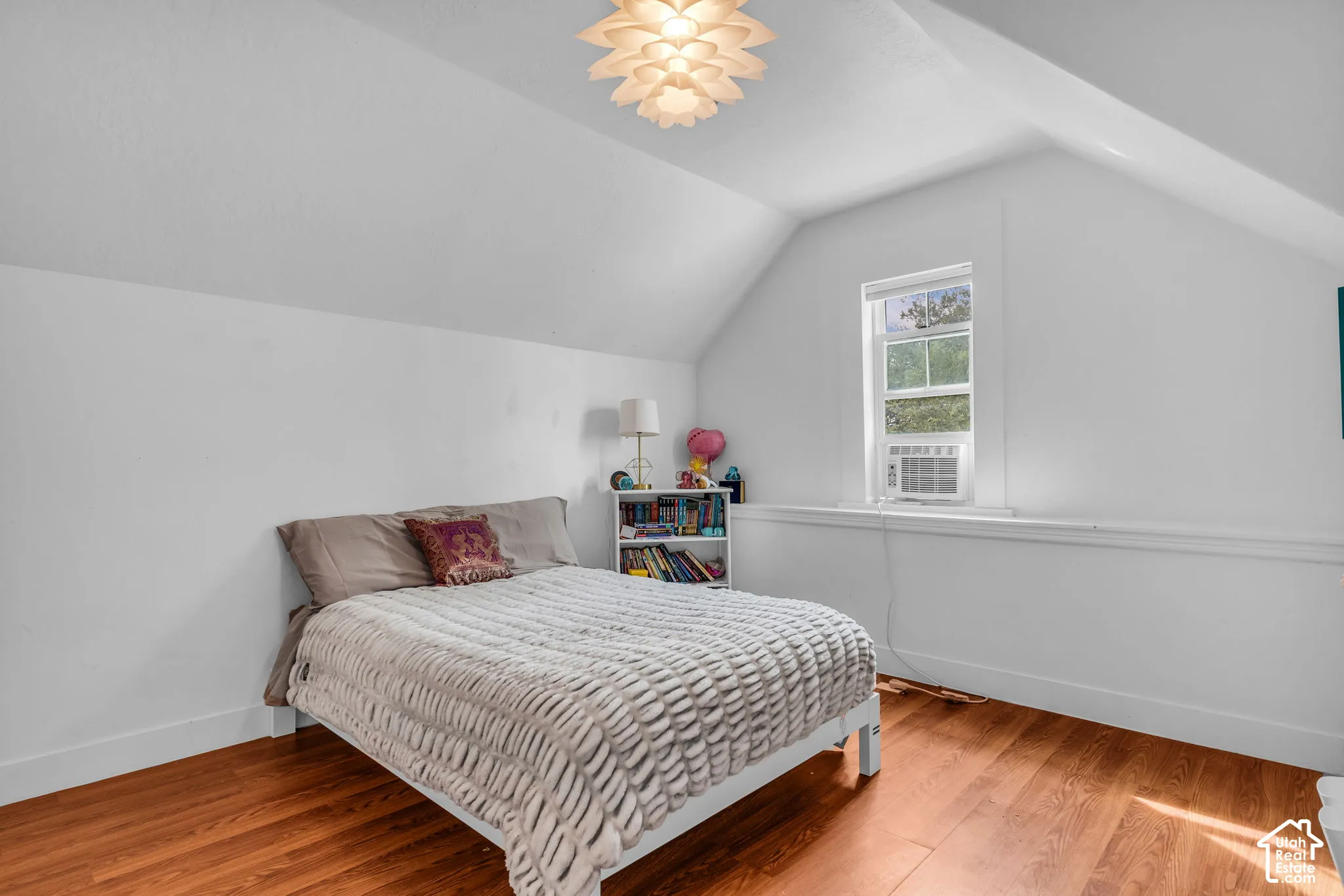 Vaulted ceiling with a decorative light fixture, warm wood-finish flooring, and a single window
