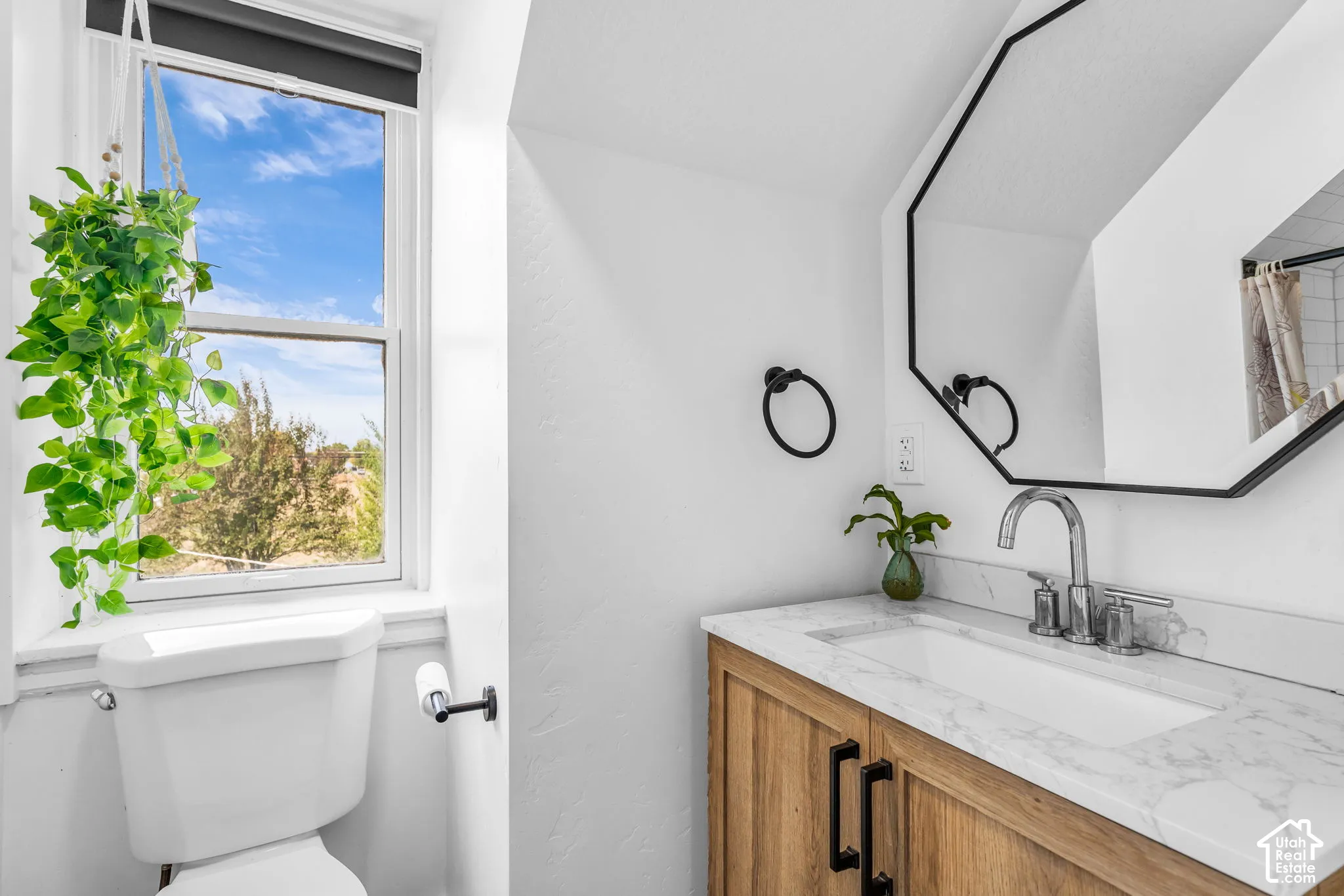 Bathroom featuring a wood-finish vanity with a white rectangular sink, a light-toned countertop, and a black-framed octagonal mirror