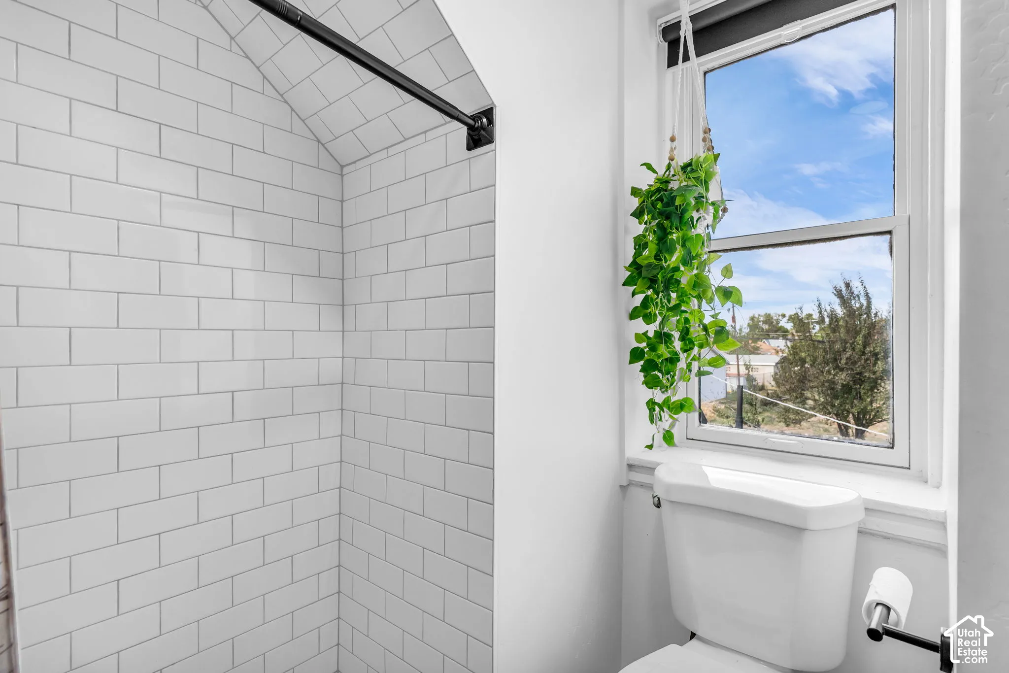 White subway tile shower enclosure with an arched ceiling and a matte black shower rod