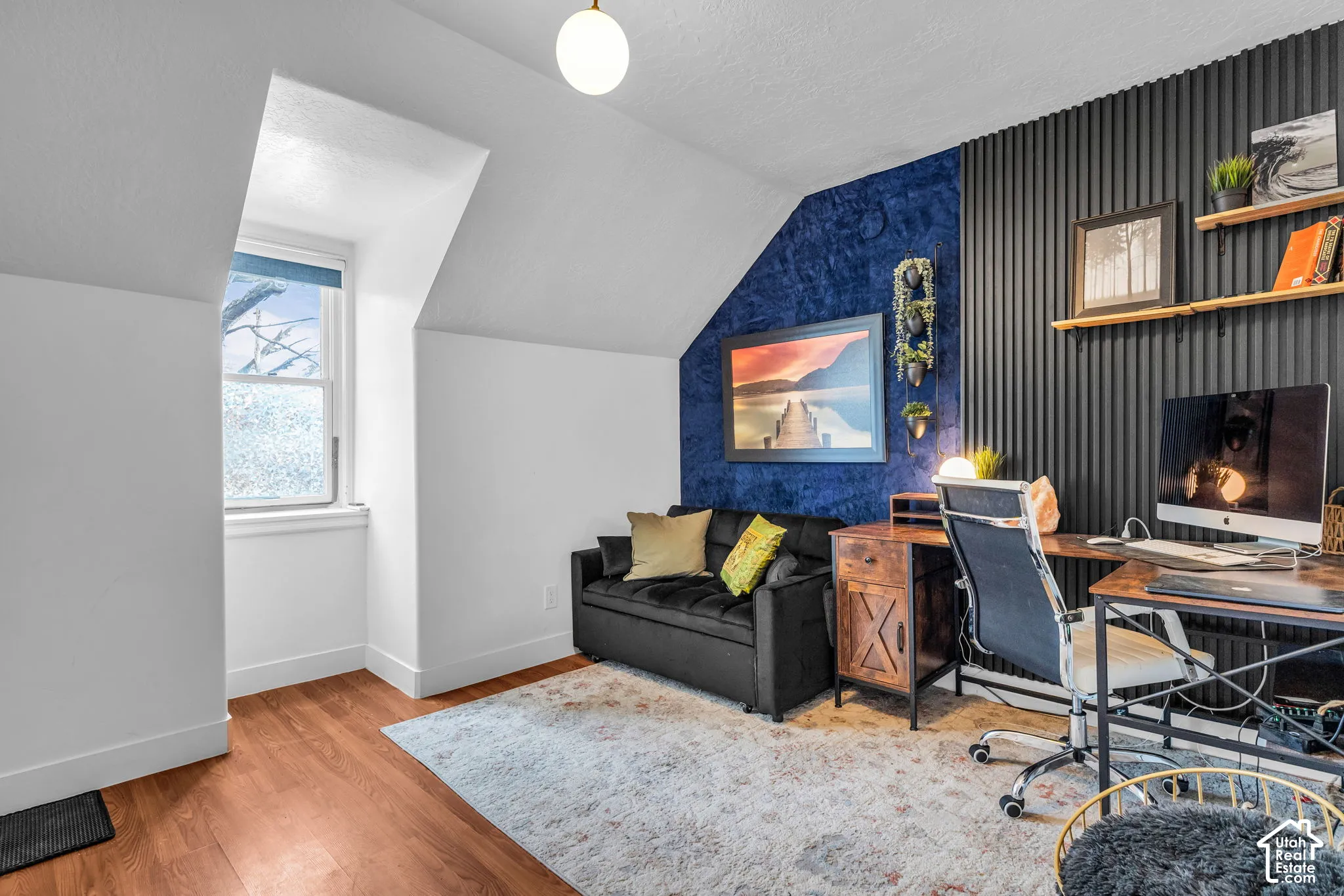 Wood-finish flooring, accent wall with vertical paneling, recessed window, sloped ceiling, and overhead spherical light fixture